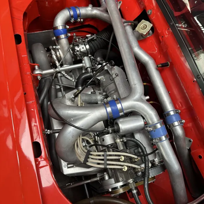 Aufgeladener Motor eines Fiat X1/9 mit Aluminiumrohren und blauen Silikonmanschetten im roten Motorraum.