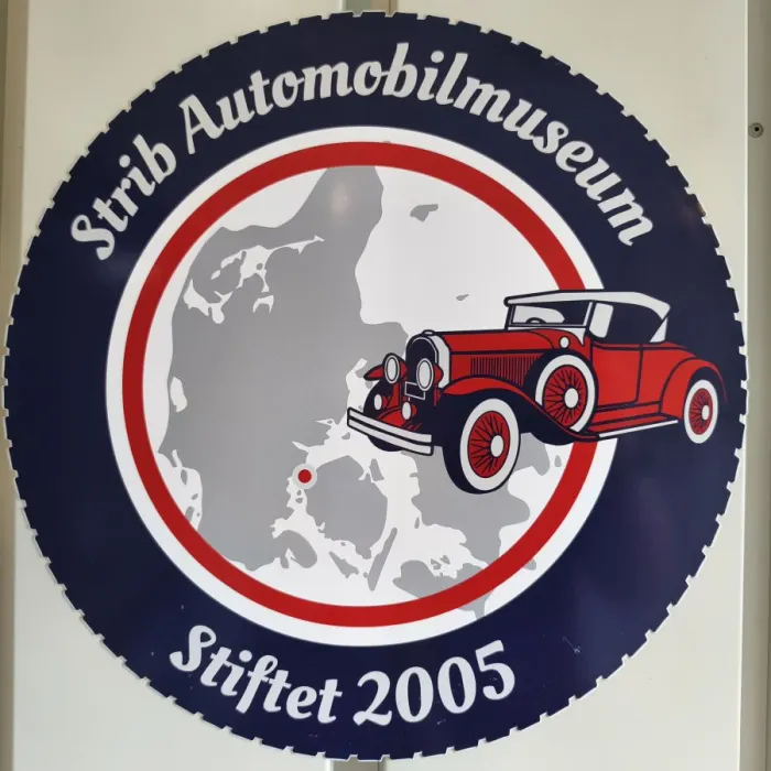 Rundes Logo des Strib Automobilmuseum, gegründet 2005, mit rotem Oldtimer vor einer Karte von Dänemark.