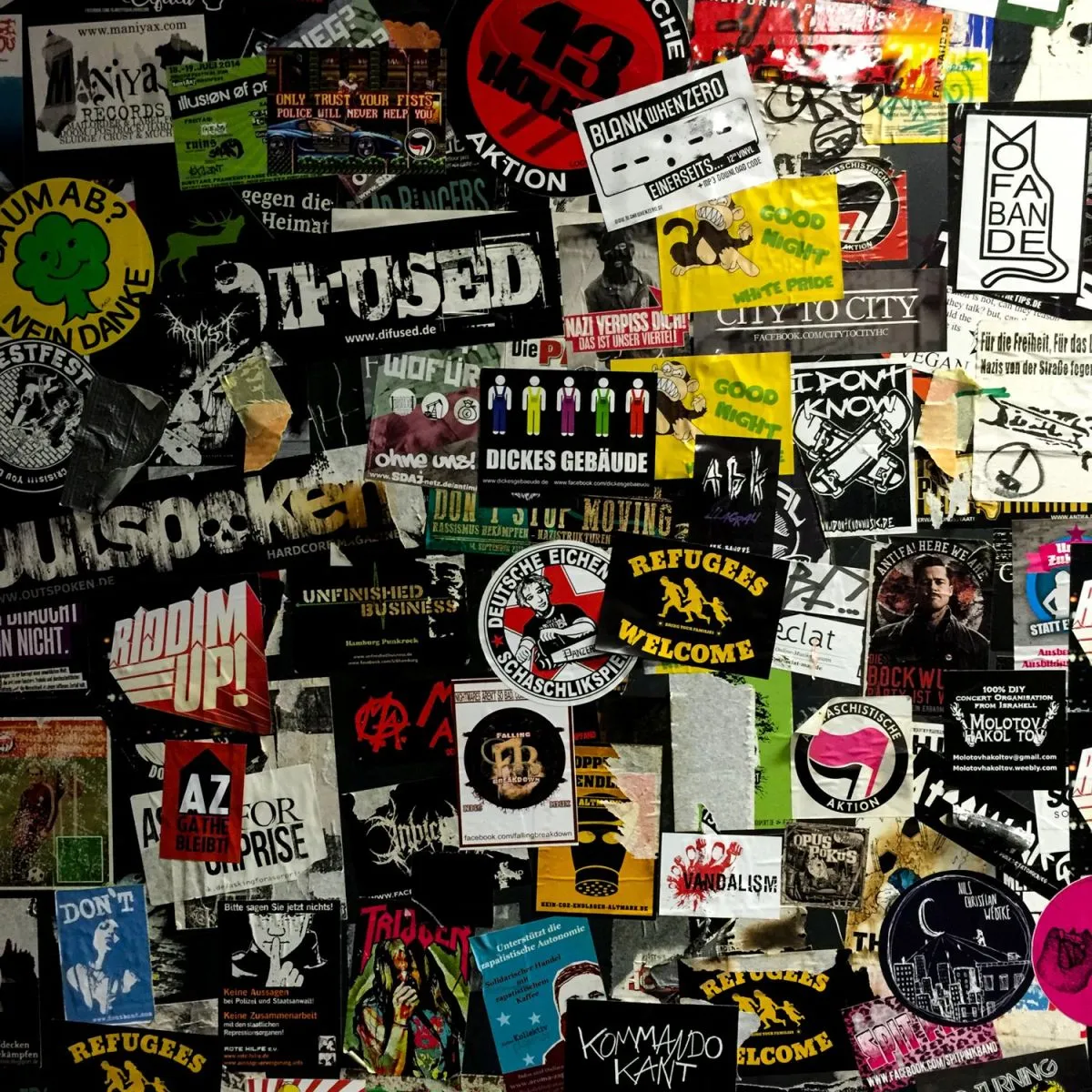 Wand, dicht beklebt mit bunten Aufklebern aus Punk- und Hardcore-Szene und linker Politik, darunter Antifa-Logos, ‚Refugees Welcome’ und Bandnamen.